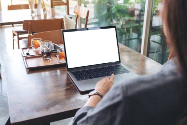 Kafedeki ahşap masadaki boş beyaz masaüstü ekranı ile laptopa dokunan bir kadının görüntüsü.