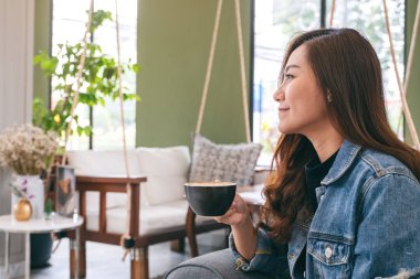 Kafede elinde sıcak kahve tutan ve içen Asyalı güzel bir kadının yakın çekimi.