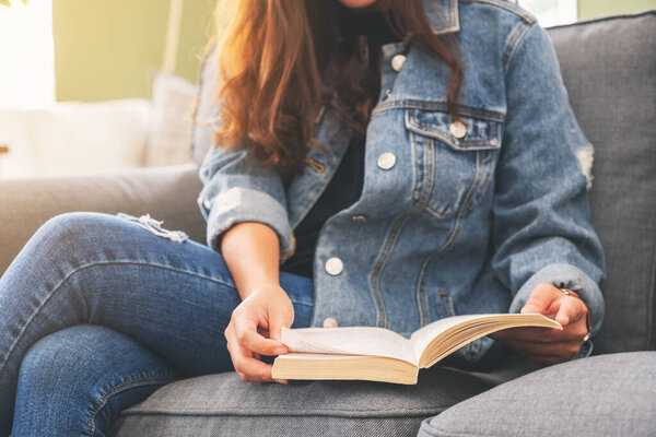 Closeup image of a woman sitting and reading a vintage novel book on sofa