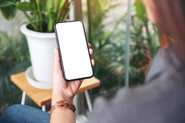 Mockup image of a woman holding and using black mobile phone with blank desktop screen in cafe