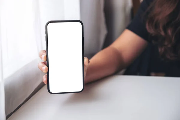 Mockup image of a woman holding and showing black mobile phone with blank screen in cafe