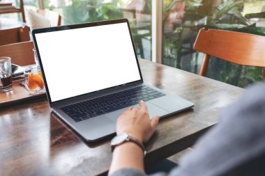 Kafedeki ahşap masadaki boş beyaz masaüstü ekranı ile laptopa dokunan bir kadının görüntüsü.