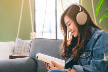 Güzel bir Asyalı kadın kitap okurken kulaklıkla müzik dinlemekten hoşlanır.