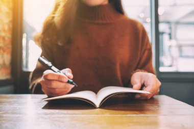 Tahta masaya dolma kalemle boş deftere yazan bir kadının yakın plan resmi.