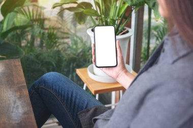 Kafedeki boş masaüstü ekranlı siyah cep telefonu tutan ve kullanan bir kadının görüntüsü