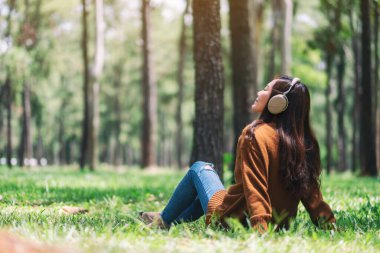Güzel Asyalı bir kadın kulaklıkla müzik dinlemekten hoşlanır. Parkta mutlu ve rahat hisseder.