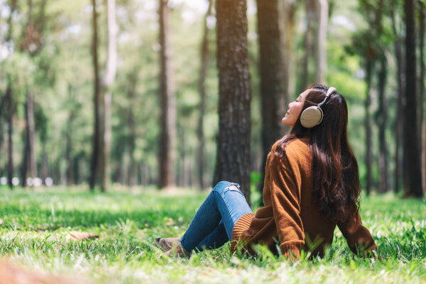 Красивая женщина с удовольствием слушает музыку в наушниках, чувствуя себя счастливой и расслабленной в парке
