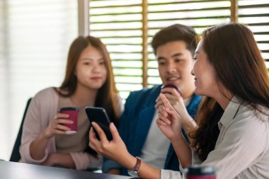 Ofiste kahve içerken aynı cep telefonuna bakan insanların yakın plan görüntüsü.