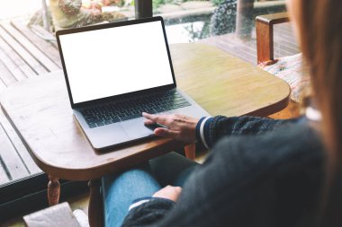 Tahta masadaki boş beyaz masaüstü ekranlı laptopa dokunan ve kullanan bir kadının görüntüsü. 