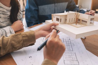 Bir grup mimar, bir mimari modeli ve ofis masasında çizim kağıtlarını tartışıyor.