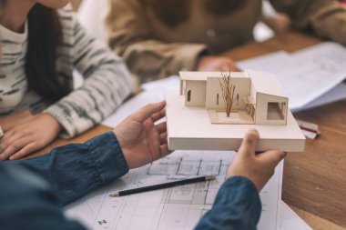 Bir grup mimar, bir mimari modeli ve ofis masasında çizim kağıtlarını tartışıyor.