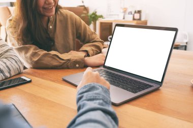 İnsanlar ahşap masadaki dizüstü bilgisayarı birlikte kullanıyorlar ve ona bakıyorlar.