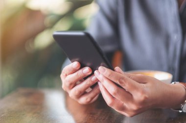 Kafe 'de elinde kahve fincanıyla cep telefonu tutan ve kullanan bir kadının yakın plan görüntüsü.