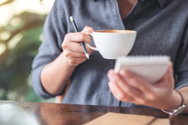 Not defteri ve kahve fincanı tutan bir kadının yakın plan görüntüsü.