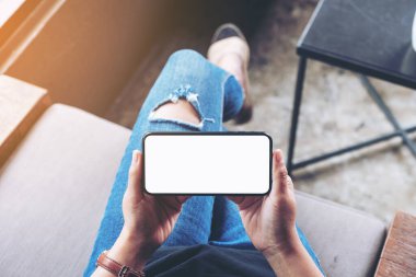 Kafede otururken elinde boş ekranla siyah cep telefonu tutan kadının üst görünüm görüntüsü