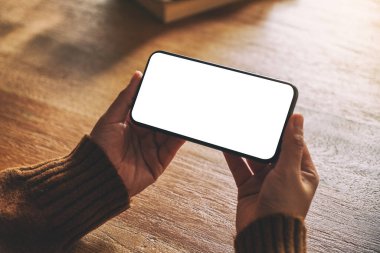 Tahta masadaki boş masaüstü ekranlı siyah cep telefonunu tutan ellerin görüntüsü