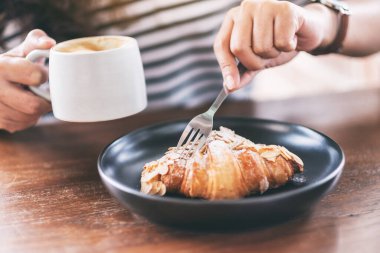 Kahve içen ve kahvaltıda çatalla kruvasan yiyen bir kadının yakın plan görüntüsü.