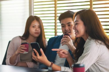 Kahve içerken aynı cep telefonuna bakan insanların yakın plan görüntüsü.