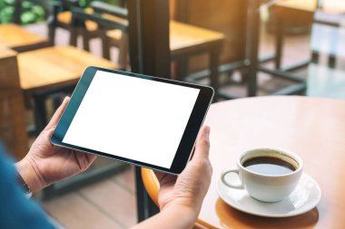 Siyah tabletli, beyaz ekranlı ve ahşap masada kahve fincanı olan ellerin görüntüsü. 