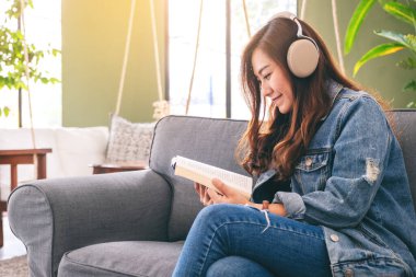 Güzel bir Asyalı kadın kitap okurken kulaklıkla müzik dinlemekten hoşlanır.