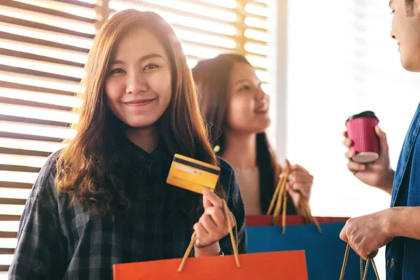 一个漂亮的亚洲女人 提着购物袋 带着一张有朋友背景的信用卡 — 图库照片