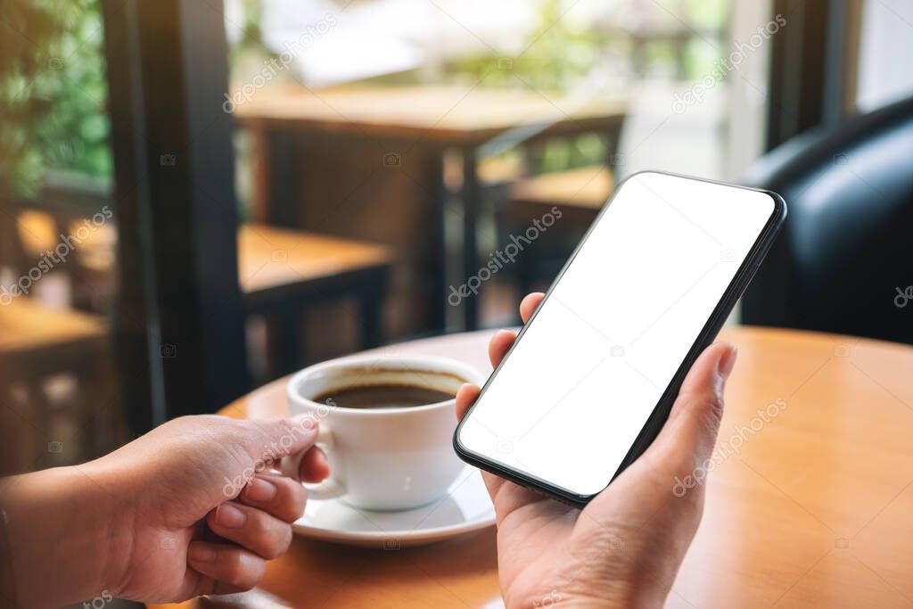 Mockup image of hands holding black mobile phone with blank desktop screen while drinking coffee