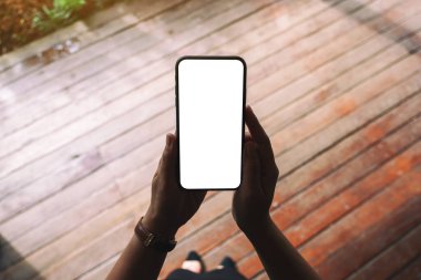 Boş masaüstü ekran ile siyah cep telefonu tutan bir kadının üst görünüm görüntüsü