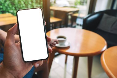 Kafede kahve içen bir kadının beyaz ekranlı, elinde siyah cep telefonu olan bir adamın görüntüsü.