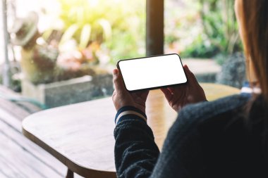 Antika kafede otururken elinde boş masaüstü ekran olan siyah bir cep telefonu tutan bir kadının görüntüsü