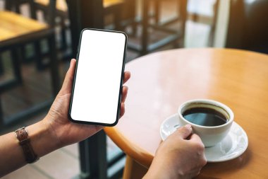 Kahve içerken ellerin siyah cep telefonunu boş masaüstü ekran ile tutuş görüntüsü 