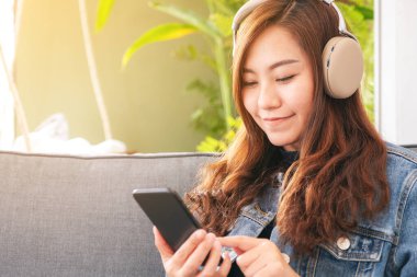 Güzel bir Asyalı kadın müzik dinlemek için cep telefonu ve kulaklık kullanıyor.