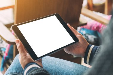 Tahta sandalyede otururken elinde boş beyaz masaüstü ekranı olan siyah tablet tutan bir kadının görüntüsü.