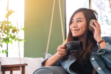Güzel bir Asyalı kadın kahve içerken kulaklıkla müzik dinlemekten hoşlanır.