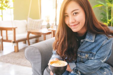 Kafede elinde bir fincan sıcak kahve tutan Asyalı güzel bir kadının yakın çekimi.