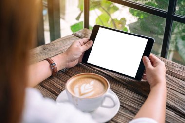 Siyah tabletli, beyaz ekranlı ve kahve fincanı tahtada olan bir kadının görüntüsü.