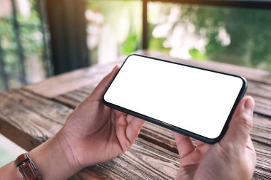 Tahta masadaki boş masaüstü ekranlı siyah cep telefonunu tutan ellerin görüntüsü