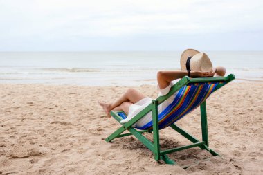 Plaj sandalyesine uzanmış, rahatlamış hisseden bir kadın.