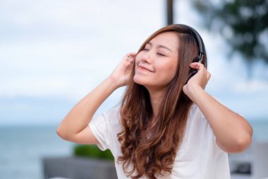 Deniz kenarında oturmuş kulaklıkla müzik dinleyen güzel bir Asyalı kadın.