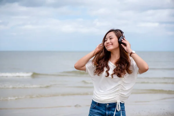 美しいアジアの女性が海のそばでヘッドフォンで音楽を聴くのを楽しむ — ストック写真