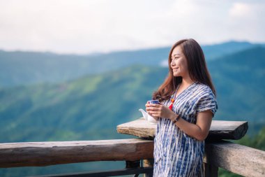 Asyalı güzel bir kadın ayakta duruyor ve yeşil dağ arka planında çay içiyor.