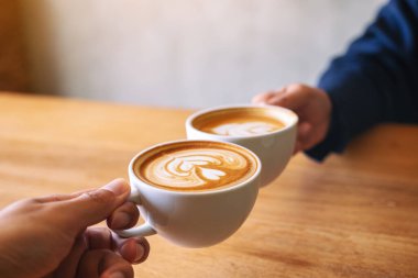 Kafe 'de iki kahve fincanını ahşap masaya tokuşturan bir adam ve bir kadının yakın görüntüsü.