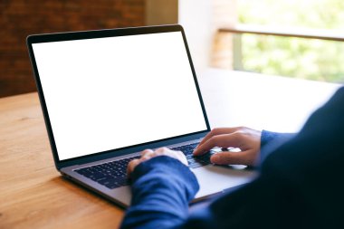 Laptop bilgisayar klavyesinde yazı yazan ve kullanan bir kadının resmi. Tahta masadaki boş beyaz masaüstü ekran. 