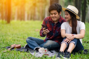 Parkta birlikte otururken cep telefonunu kullanan ve ona bakan genç bir çift.