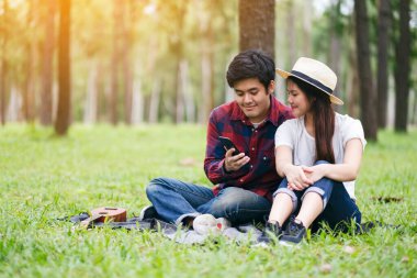 Parkta birlikte otururken cep telefonunu kullanan ve ona bakan genç bir çift.