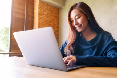Asyalı bir kadının ahşap masada dizüstü bilgisayarda çalışıp daktilo yazarken yakın plan görüntüsü.