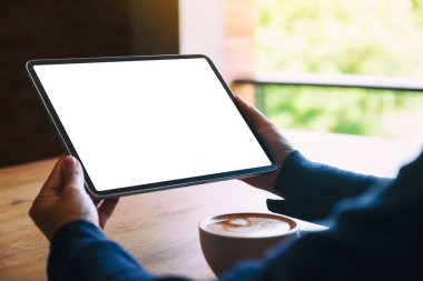 Siyah tabletli, beyaz ekranlı ve ahşap masada kahve fincanı olan bir kadının görüntüsü.