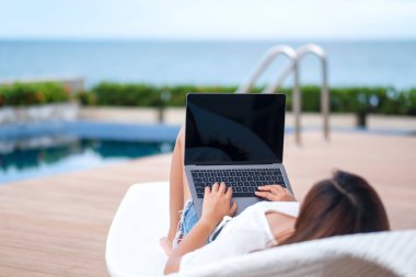 Yüzme havuzunda yatarken boş beyaz ekranla dizüstü bilgisayar kullanan ve yazan bir kadın.