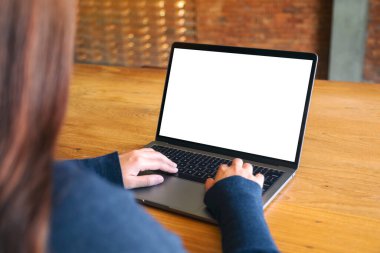 Laptop bilgisayar klavyesinde yazı yazan ve kullanan bir kadının resmi. Tahta masadaki boş beyaz masaüstü ekran. 