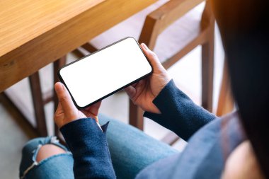 Kafede elinde siyah cep telefonu olan beyaz ekranlı bir kadının görüntüsü.