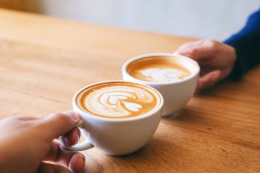 Kafe 'de iki kahve fincanını ahşap masaya tokuşturan bir adam ve bir kadının yakın görüntüsü.